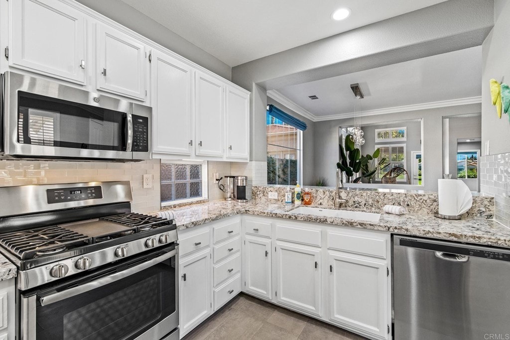 The kitchen features modern appliances, including a stainless-steel gas range and dishwasher. White cabinetry contrasts with the granite countertops. Large windows allow natural light, showcasing an inviting atmosphere and a view of the outdoor space.