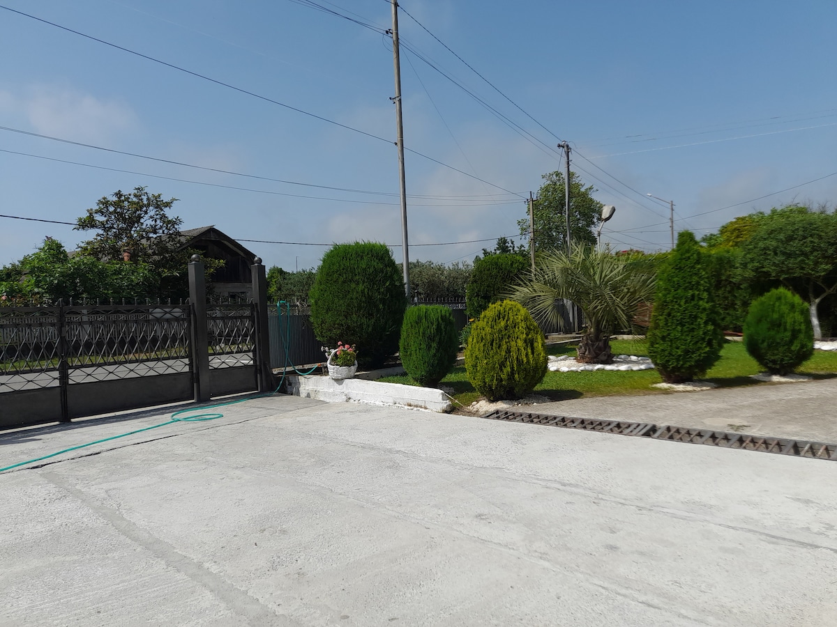 A well-maintained outdoor space features landscaped greenery, including neatly trimmed bushes and trees. A paved driveway leads into the area, complemented by a fence that outlines the property. Clear skies enhance the inviting setting.