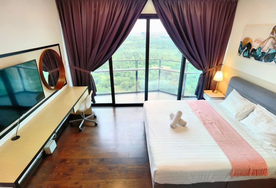 A spacious bedroom features large windows offering expansive views of the surrounding landscape. A comfortable bed is paired with a soft blanket. A sleek desk and chair are positioned beside the window, complemented by a wall-mounted television and a round mirror.