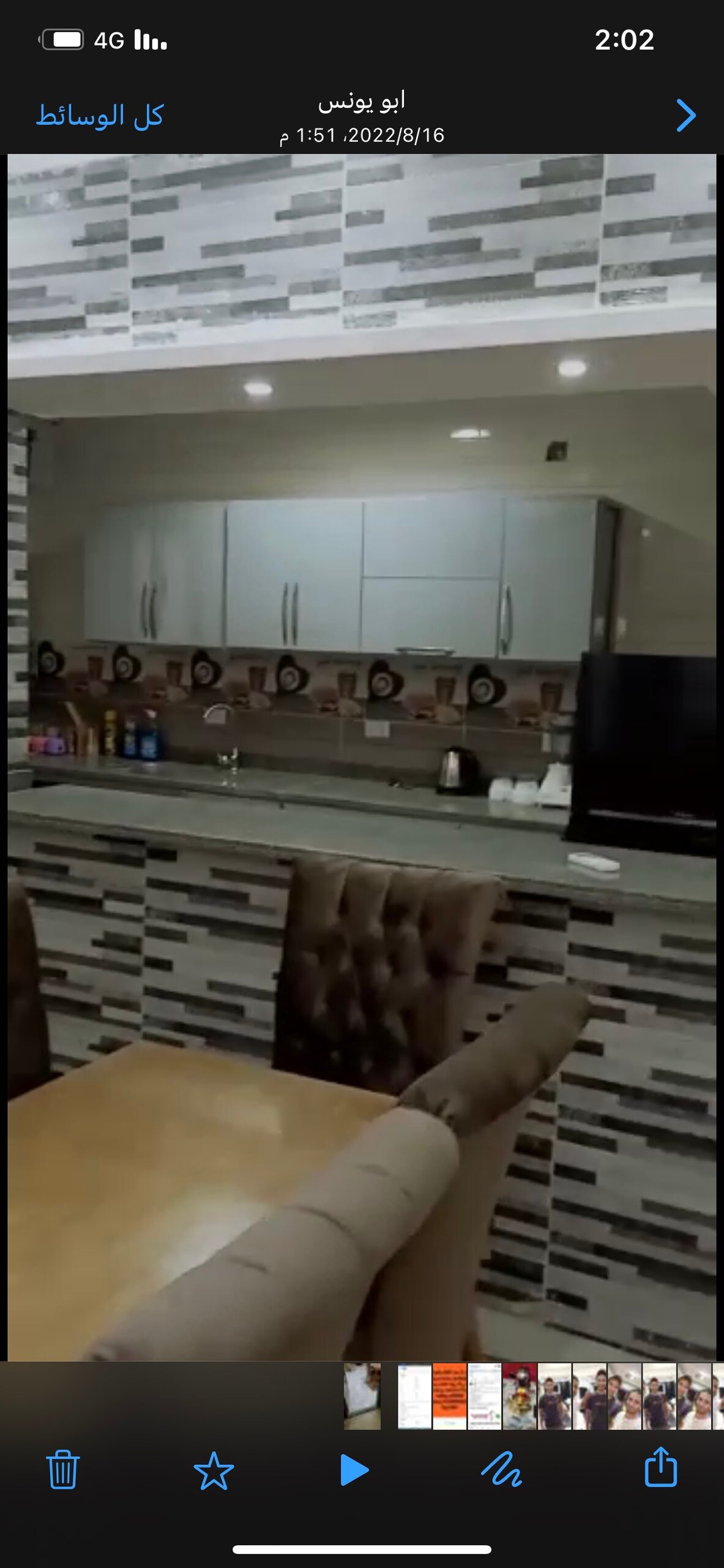 A modern kitchen features sleek cabinetry and a large countertop, equipped with various kitchen appliances. A dining area is visible, highlighted by plush chairs surrounding a wooden table. Neutral tones and contemporary design elements create a cohesive look.