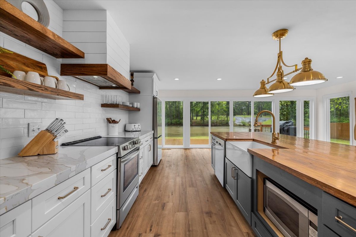 A modern kitchen features an open layout with ample cabinetry and wood countertops. Stainless steel appliances are present, including a gas range. A large window allows natural light to fill the space, with a view of the backyard and nearby trees.