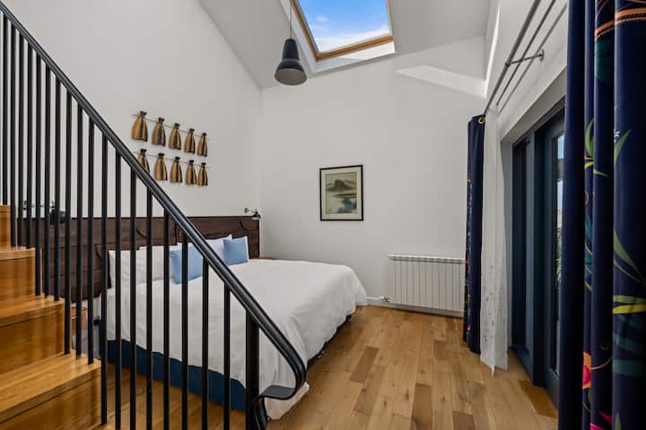 מיטת סופר קינג בסוויטת חדר השינה הראשי בקומת הקרקע. אפשר לסדר את המיטה כמיטות נפרדות. גרם מדרגות שמוביל לאזור ישיבה פרטי בקומת ביניים.
דלתות צרפתיות נפתחות למרפסת.