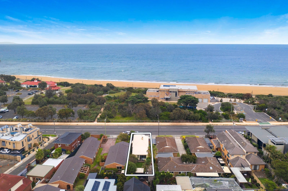An aerial view captures the proximity of the Edwardian home to Mordialloc Beach. Sandy shores stretch along the coastline, while the neighborhood features well-maintained houses, gardens, and the main road leading to the beach, creating a vibrant beachside community.