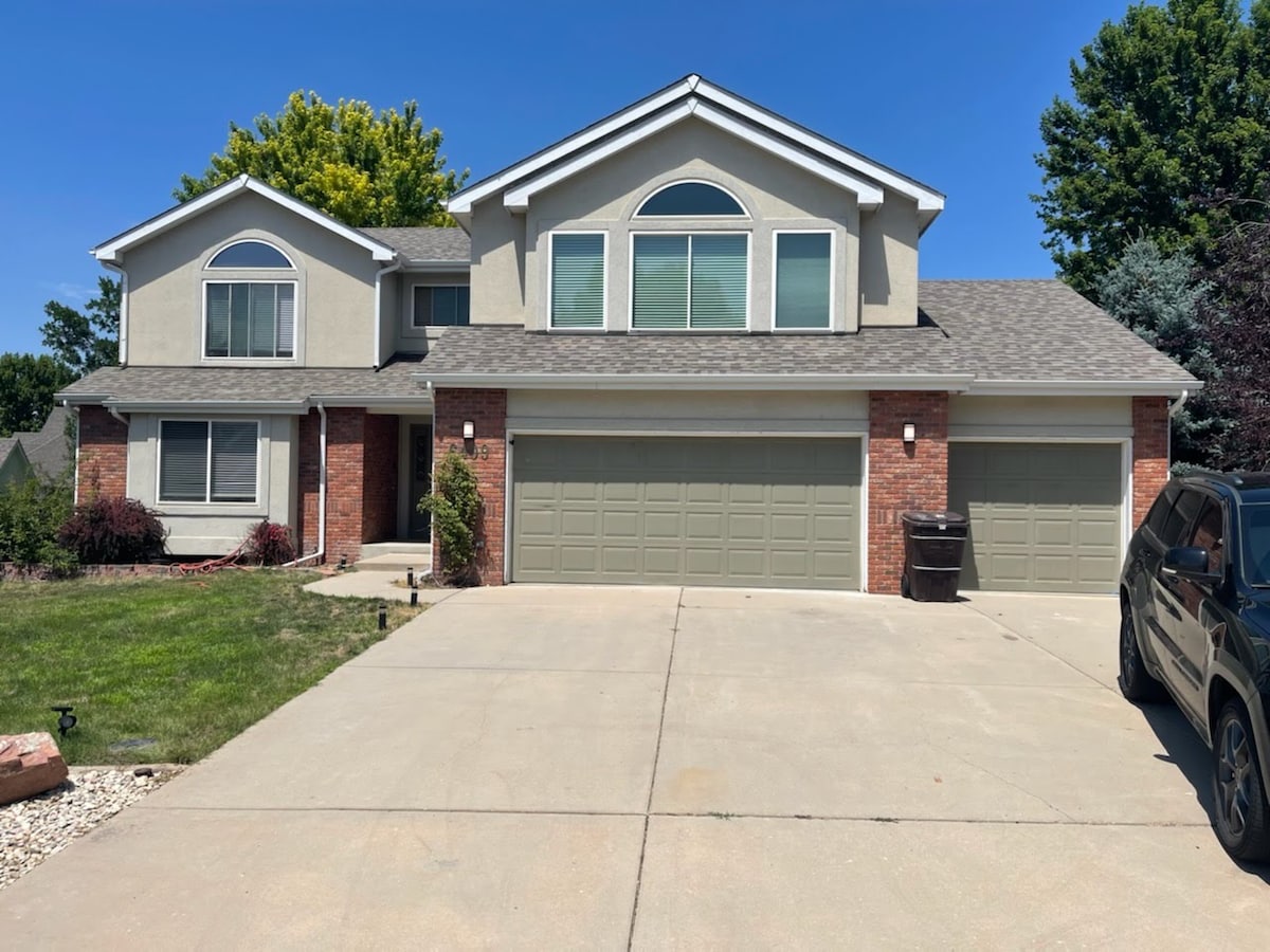 The exterior of the house showcases a two-story design with a combination of brick and stucco, complemented by large windows and a vaulted roof. A spacious driveway leads to the three-car garage, surrounded by well-maintained lawn and landscaping.