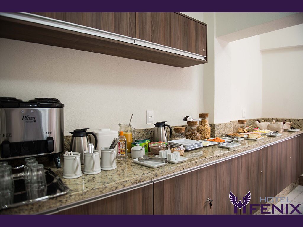 A breakfast area is presented with a granite countertop displaying a variety of food options. Coffee machines, juice containers, and an assortment of jars can be seen alongside stackable dishes and glasses. The atmosphere is organized and inviting for guests.