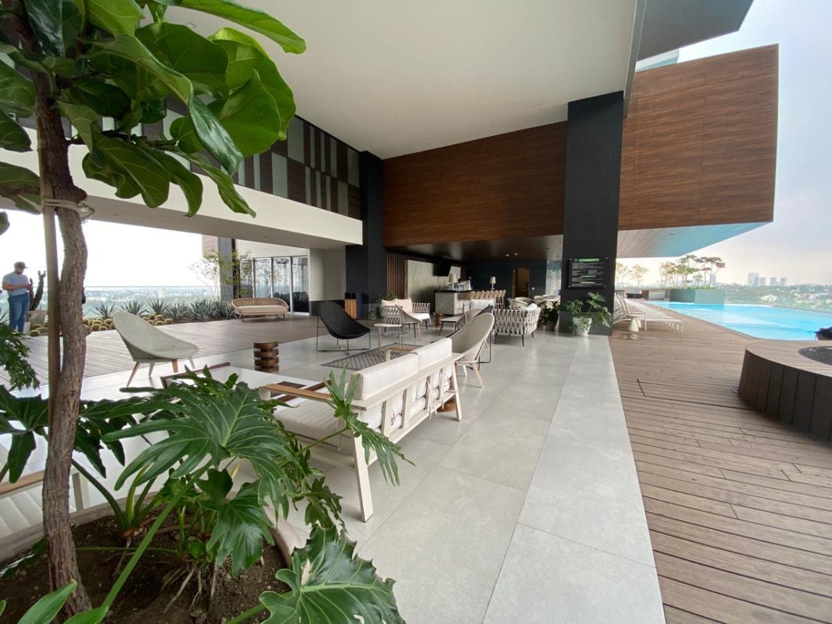 A spacious outdoor lounge area is complemented by contemporary furnishings. Comfortable seating arrangements surround a central space, offering views of the surrounding greenery. A sleek pool can be seen in the background, while a mix of plants adds a natural touch to the modern design.