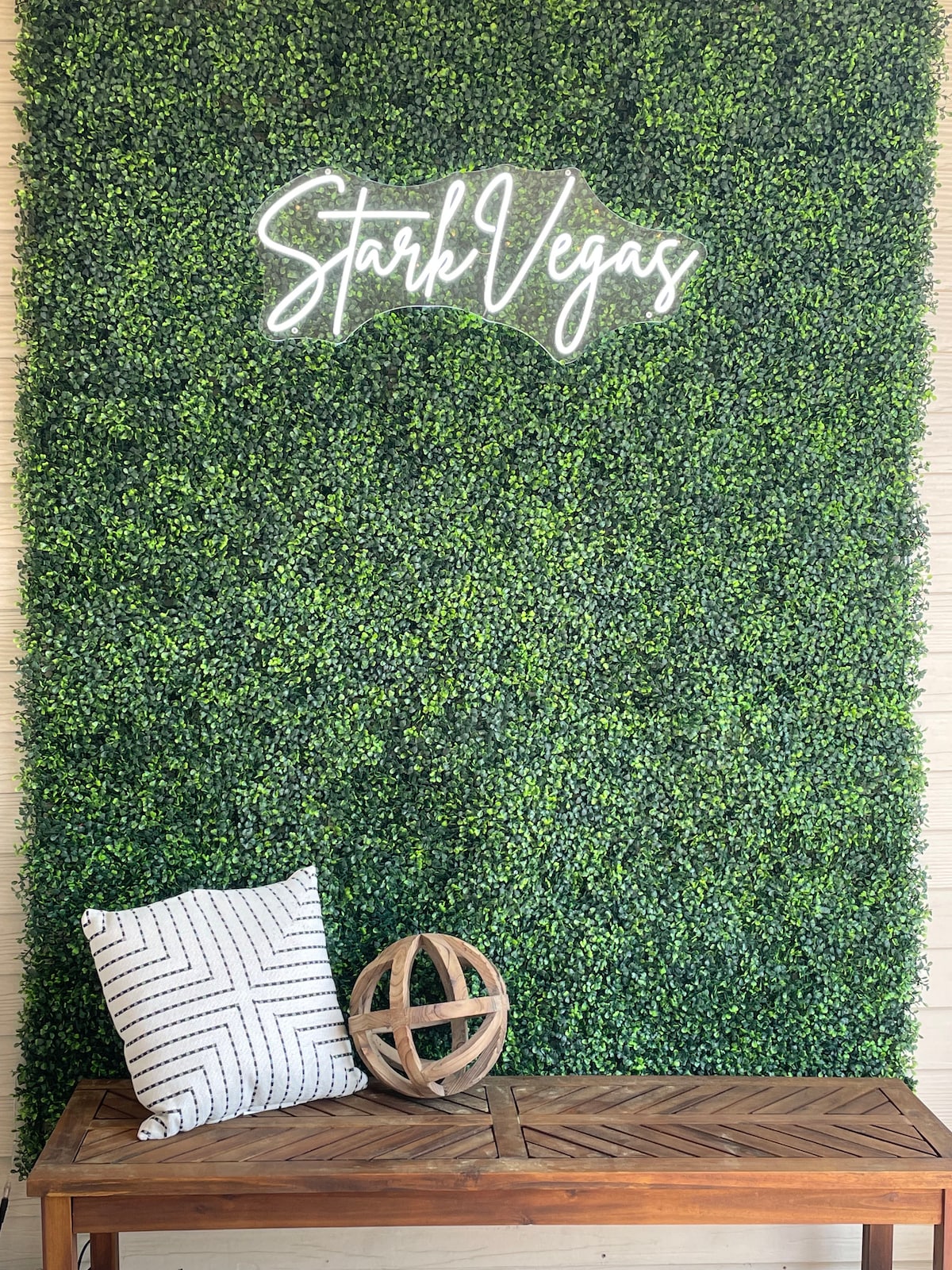 A decorative green wall serves as a backdrop, complemented by a wooden bench. A patterned pillow is placed on the bench, and a wooden globe decoration rests nearby, creating a welcoming entryway ambiance.
