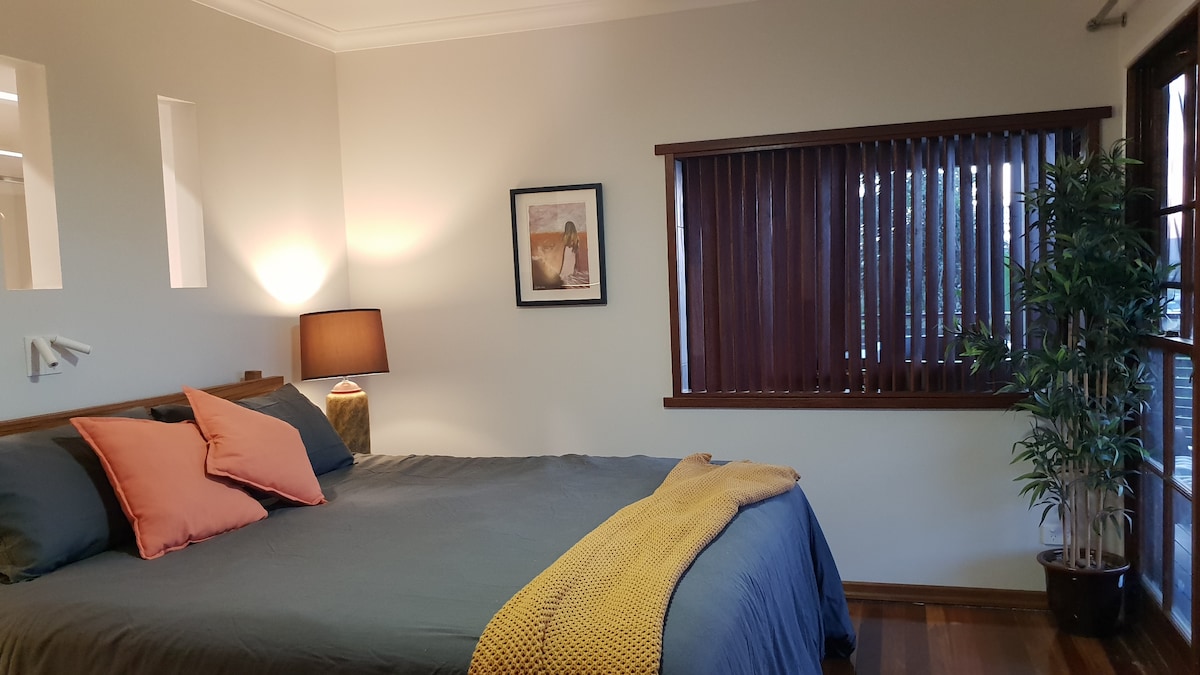 Master bedroom, with WIR behind the bedhead, glimpses of the ensuite bath behind the timber slats and mountain ranges and city skyline in the distance.