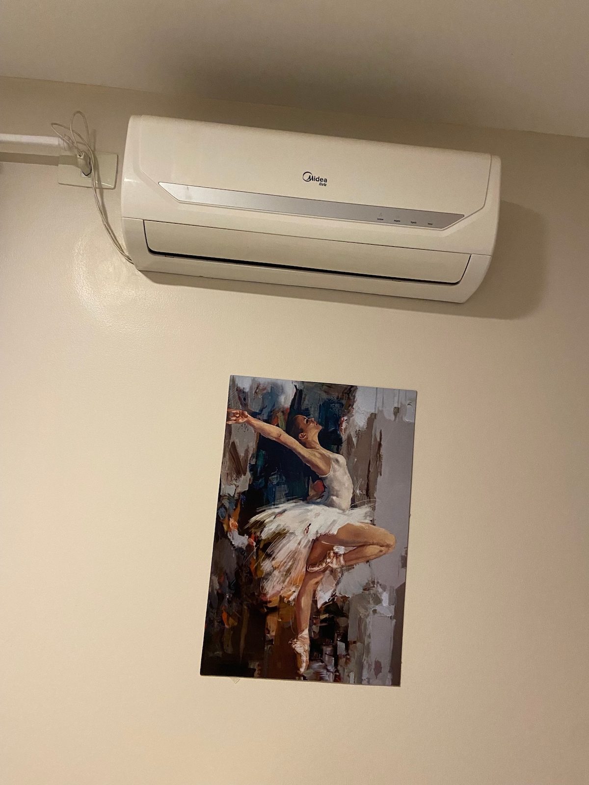 A wall-mounted air conditioning unit is positioned above a vibrant piece of artwork depicting a dancer in motion. The artwork, featuring muted tones, adds an artistic touch to the room's modern aesthetic.