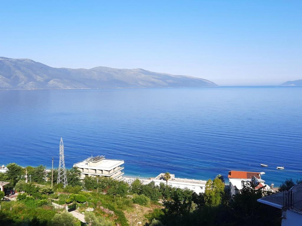A panoramic view of the serene coastline is displayed, featuring calm blue waters meeting a clear sky. A few boats are visible on the water, while lush greenery and buildings line the shore, creating a harmonious coastal scene.