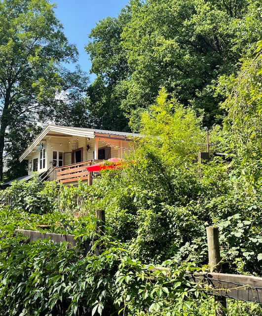 A charming chalet is nestled among lush greenery, featuring a wooden deck with a vibrant red umbrella. Sunlight filters through the surrounding trees, creating a serene atmosphere that highlights the natural setting.