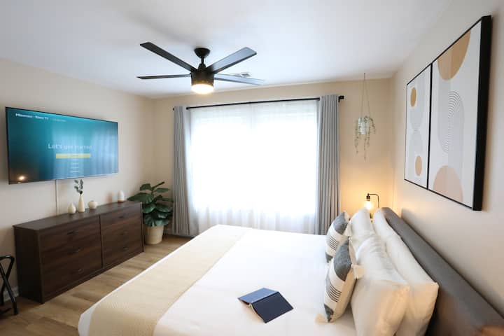 Wake up to soft morning light. Our spacious bedroom offers a clean, airy sanctuary with twin bedside lamps and plenty of room to stretch out and relax.