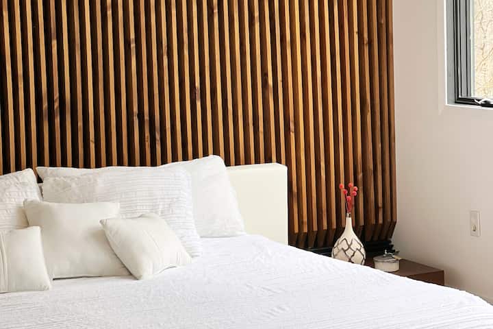 חדר שינה ראשי עם קיר נוי עשוי עץ ומיטת קינג. 