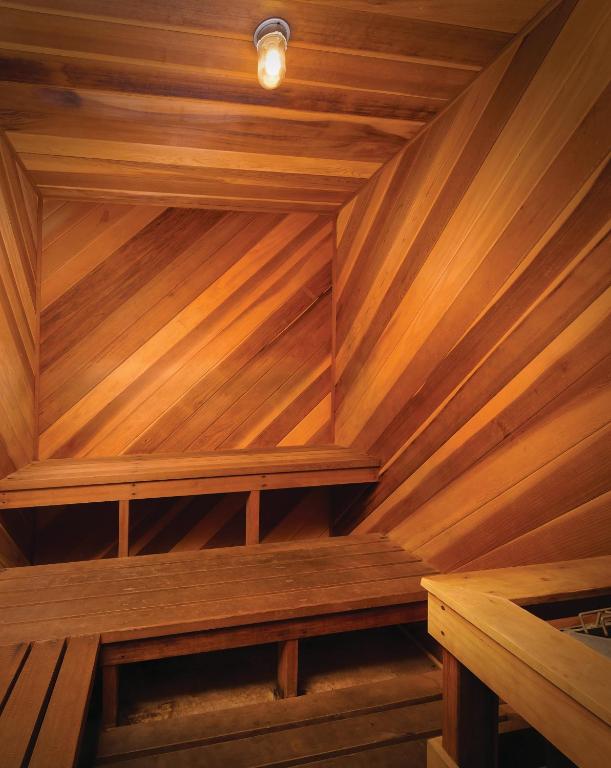 The image showcases the interior of a sauna, featuring warm wood paneling with diagonal lines. Two wooden benches provide seating against the walls, creating a cozy environment. A single light bulb illuminates the space, enhancing the tranquil atmosphere.