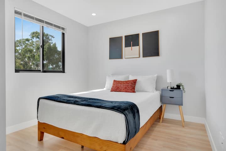 Bedroom 6: Queen bed with natural sunlight, closet space, and a night stand.