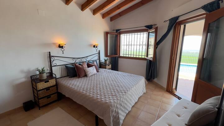 توفر غرفة النوم الرئيسية إمكانية الوصول المباشر إلى منطقة خارجية، على الأرجح شرفة أو تراس، مما يكشف عن إطلالات على حمام السباحة. تتميز بسرير مزدوج كبير مع لوح أمامي مزخرف وطاولات بجانب السرير ونافذة للضوء الطبيعي.