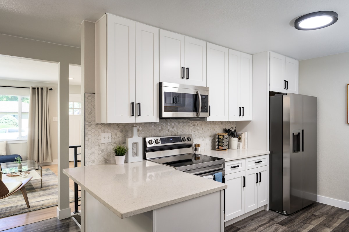 A modern kitchen features clean white cabinetry, stainless steel appliances, and a spacious countertop. Natural light fills the area, highlighting the decorative backsplash. The design emphasizes functionality and style, perfect for meal preparation and social gatherings.