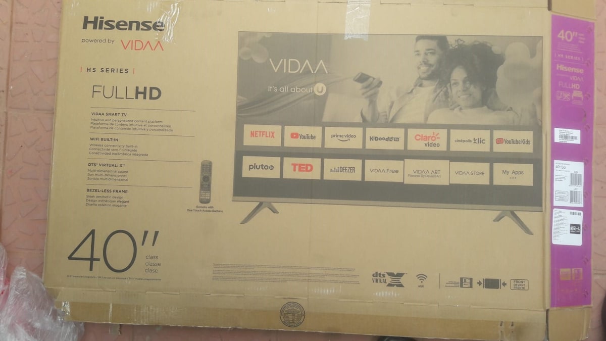 A 40-inch Hisense TV box is displayed, featuring a list of available streaming services and apps, including Netflix and YouTube. The box is positioned on a tiled floor, with the remote control visible beside it.