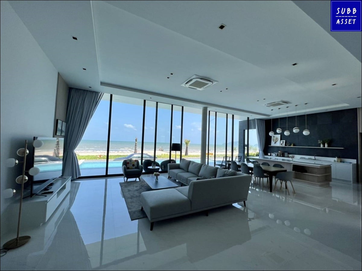 A modern living area features large glass windows that provide an expansive view of the outdoor landscape. The space is furnished with a comfortable gray sofa, a stylish coffee table, and a sleek entertainment unit. Natural light fills the room, enhancing its bright and airy atmosphere.