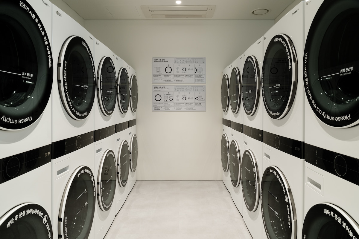A clean and functional laundry room is presented, featuring several white washing machines and dryers arranged in neat rows. Clear signage on the wall provides instructions and features a simple layout to facilitate ease of use.