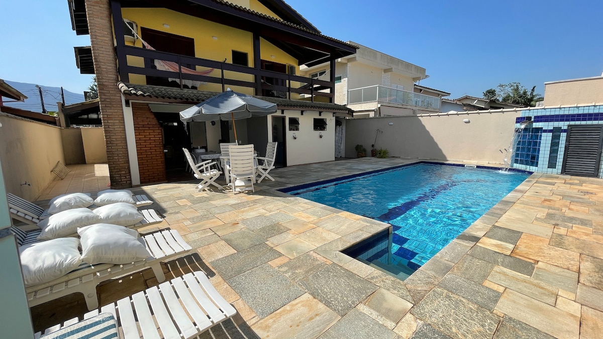 A private outdoor area features a spacious pool surrounded by patterned stone tiles. Sun loungers equipped with cushions are positioned near the pool, alongside patio furniture, including a table and umbrella for shade.