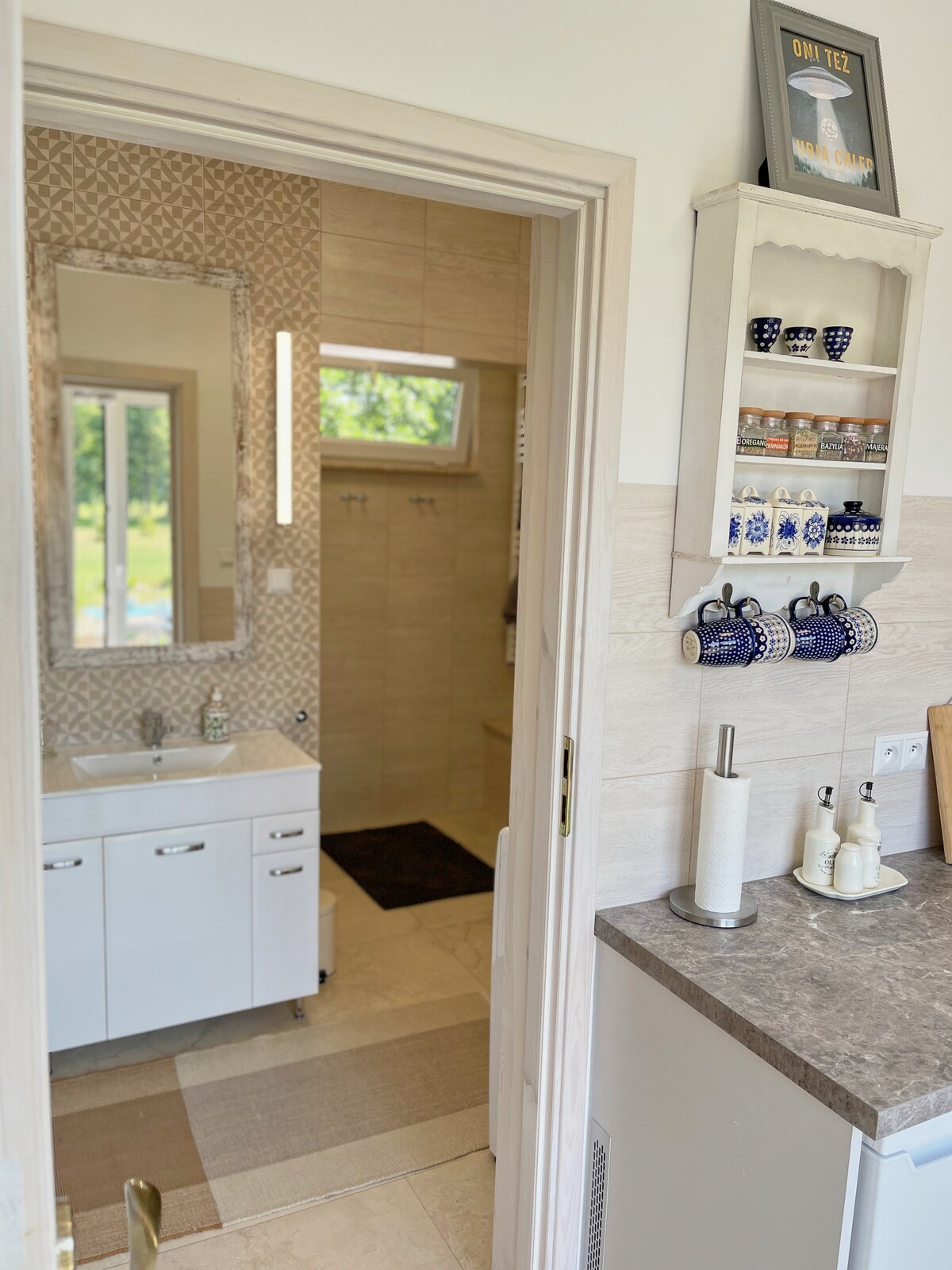 The bathroom features a modern design with a wall-mounted sink and ample storage space. Natural light enters through a window, illuminating the space. Accessories, including decorative cups and toiletries, are neatly arranged on a shelf, enhancing the room's functionality.