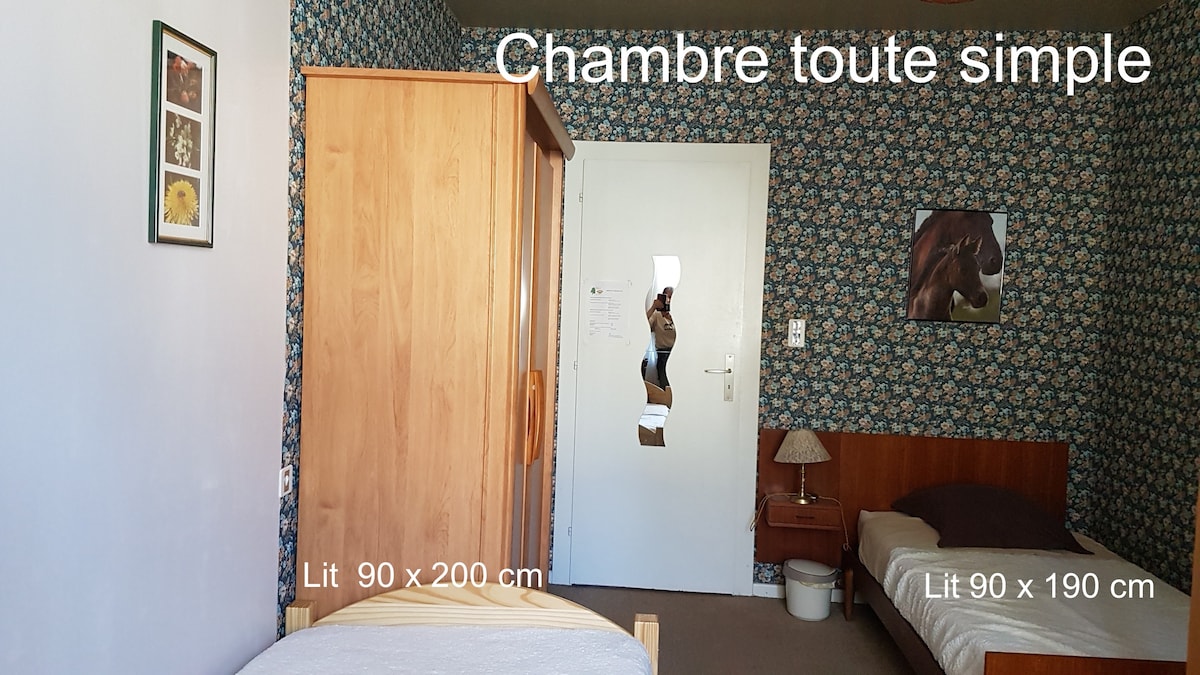 The room features two simple beds, one measuring 90 x 200 cm and the other 90 x 190 cm, accompanied by a wooden wardrobe. The walls are adorned with floral wallpaper, and a small bedside lamp is positioned next to the second bed.