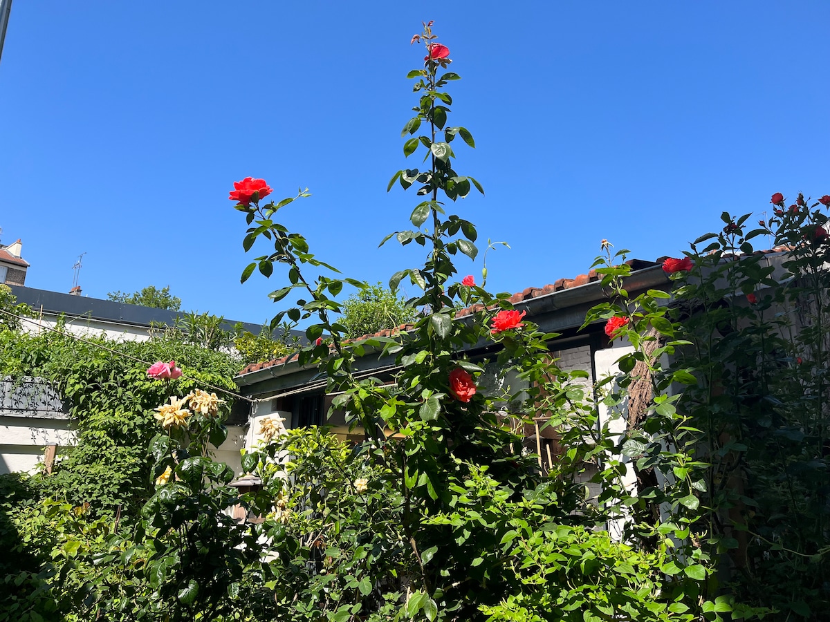 A garden view showcases tall rose bushes with vibrant red flowers against a bright blue sky. Lush greenery surrounds the area, creating a serene outdoor space that reflects the charm of the property.