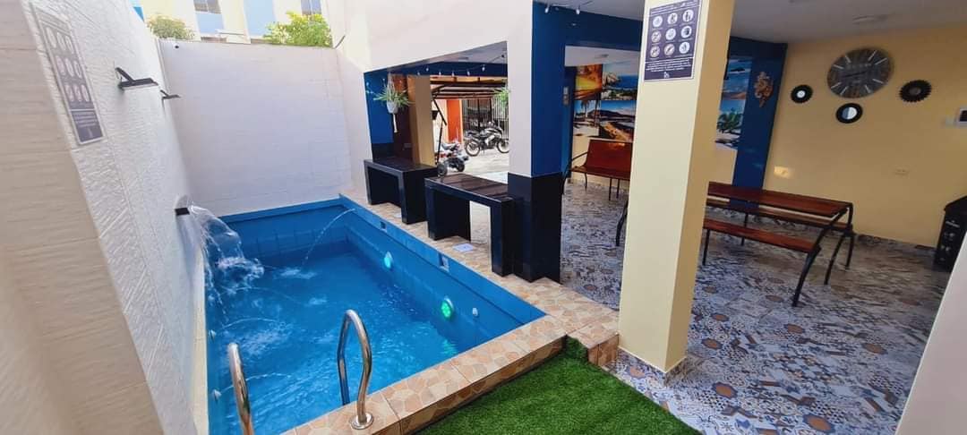 A private pool is situated beside a patio area, featuring a small waterfall and illuminated with colorful lights. Nearby, seating arrangements with black tables and benches are visible, enhancing the communal space. Decorative tiles cover the floor, adding texture and interest.