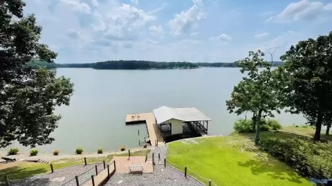 A view from the property showcases Weiss Lake, with calm waters reflecting the sky. A private dock extends into the water, providing access for boating and fishing. Lush green lawns surround the area, enhancing the natural setting.