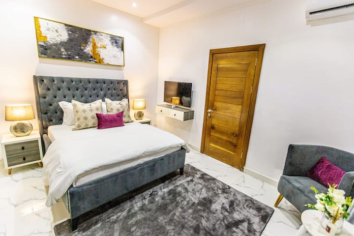 Une chambre sereine avec un lit queen confortable, des draps doux, un éclairage chaleureux et un décor de bon goût. Les grandes fenêtres invitent la lumière naturelle, créant une atmosphère calme et reposante, parfaite pour se détendre après une longue journée.