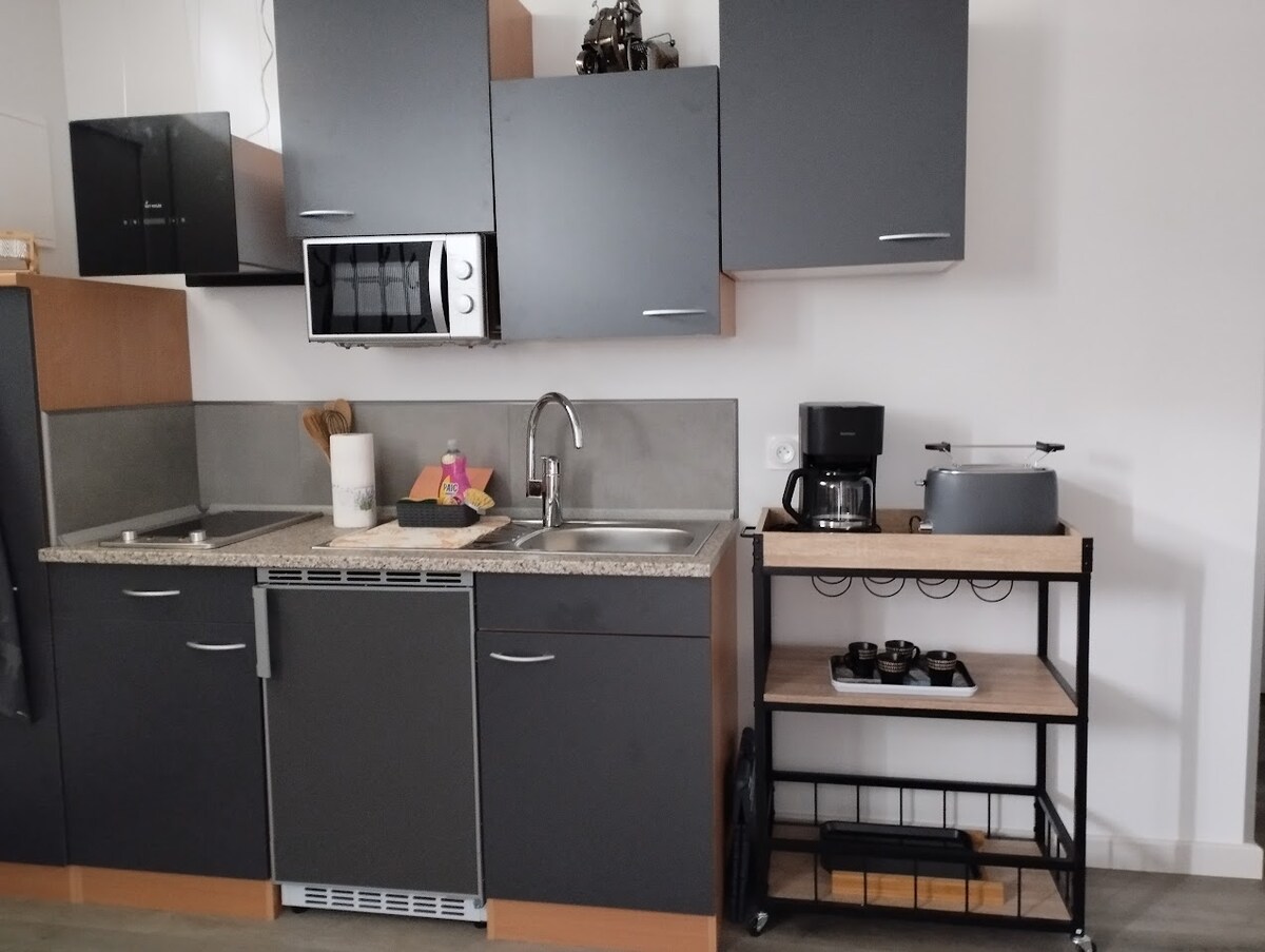 The modern kitchen is equipped with sleek cabinets and a granite countertop. Essential appliances, including a microwave and coffee maker, are visible. A compact cart provides additional storage and space for a variety of kitchen utensils, creating a functional cooking area.