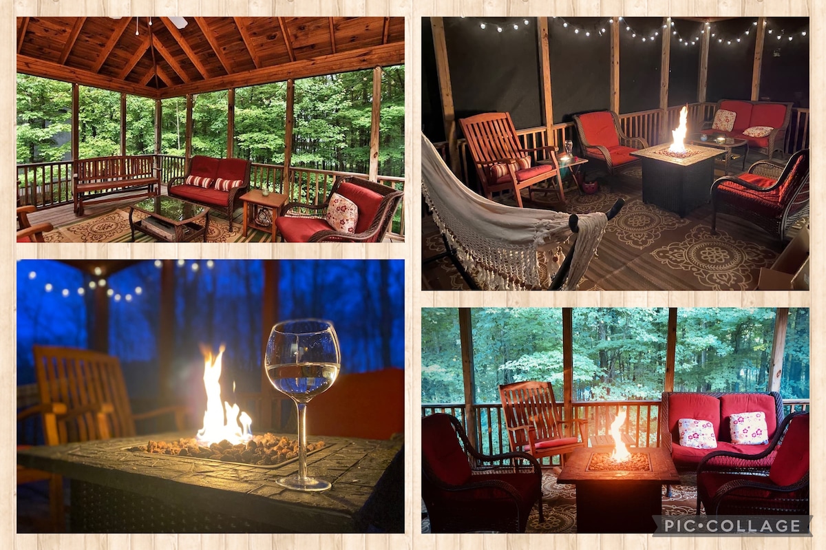 A screened-in porch showcases comfortable seating arrangements with cushions, surrounded by treetops. A fire pit serves as a centerpiece, creating an inviting space. Soft lighting from string lights enhances the ambiance, while a glass sits nearby, reflecting the warmth of the flames.