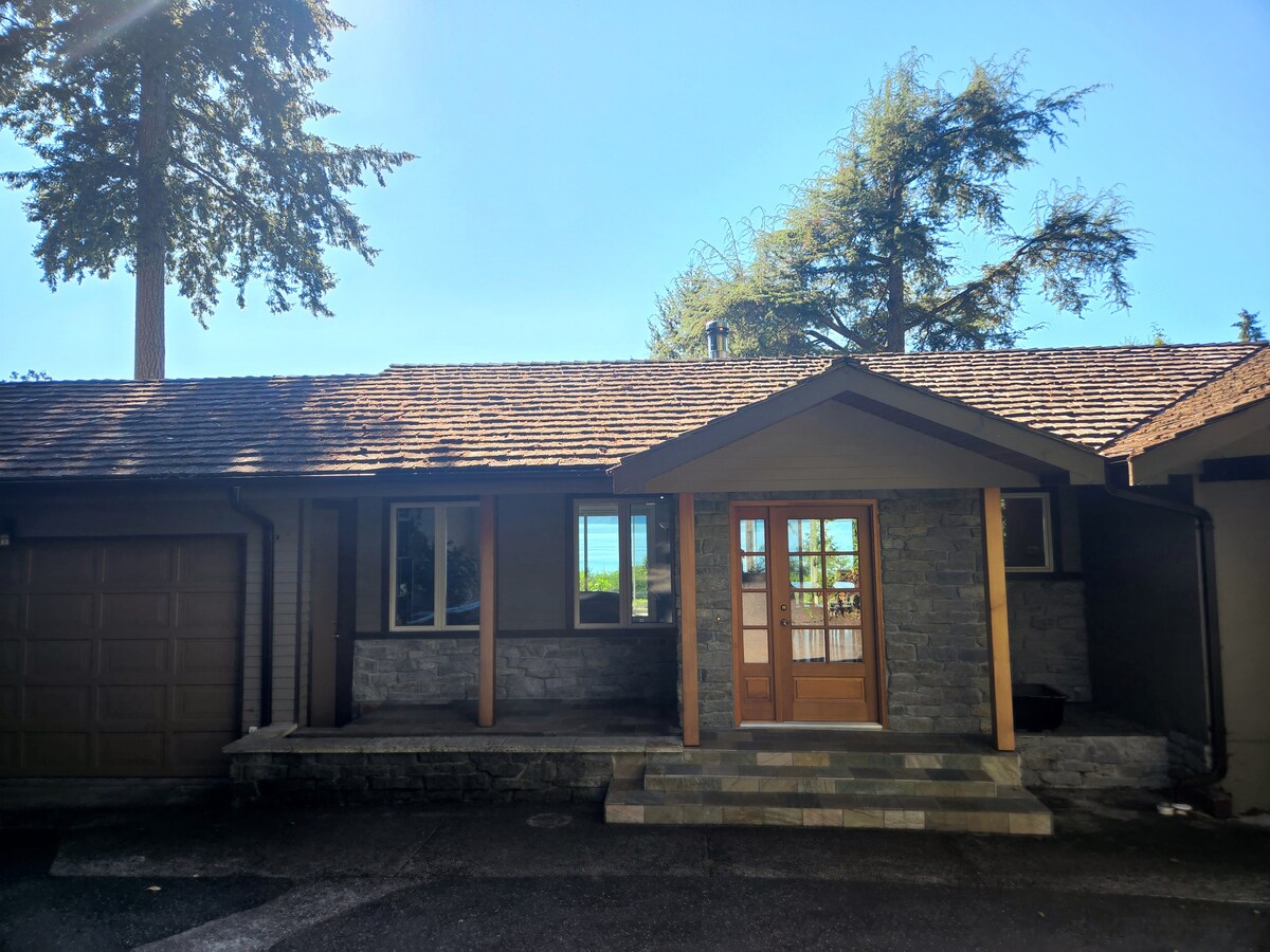 The front exterior of the property is presented with a blend of stone and wood. A stone pathway leads to double wooden doors framed by large windows, allowing natural light to enter. Surrounding trees offer a sense of privacy and tranquility.