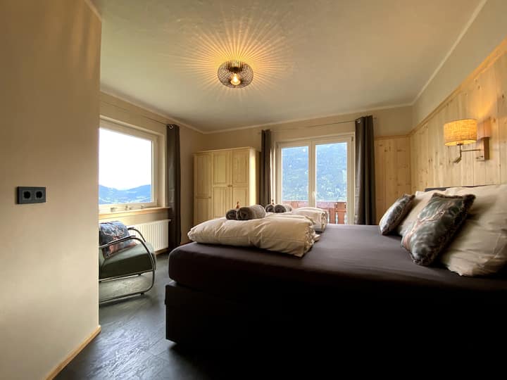 Просторната двойна спалня с пружинно легло KingSize Box, фотьойл и гардероб. От спалнята се разкрива спираща дъха гледка към долината, езерата и планините. През френските врати влизате в просторния балкон с южно изложение.