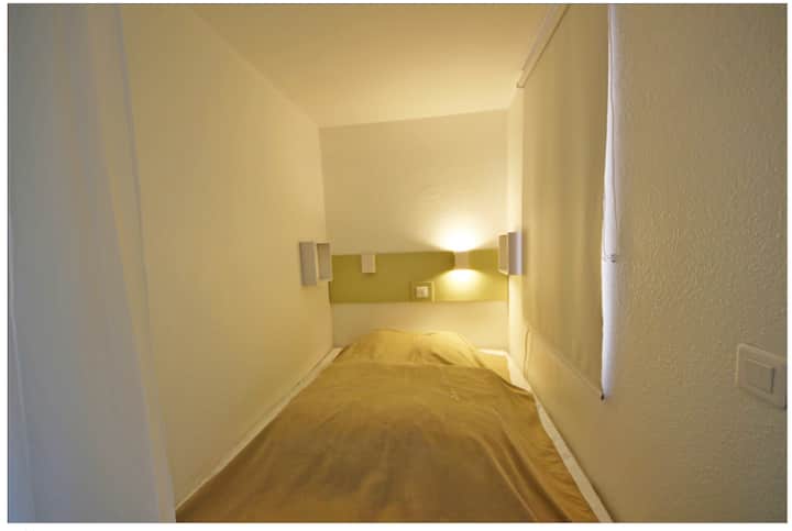 חדר שינה בבקתה עם מיטה זוגית לאחרונה. מזרן לאחרונה (2 שנים). חלון המשקיף על מסדרונות הבניין.