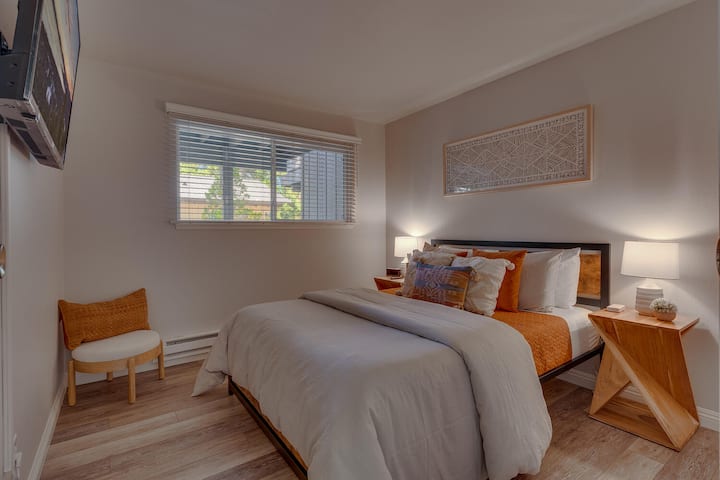 Relax in this cozy queen bedroom featuring warm orange accents, stylish wood furnishings, and a Smart TV for winding down at the end of the day.