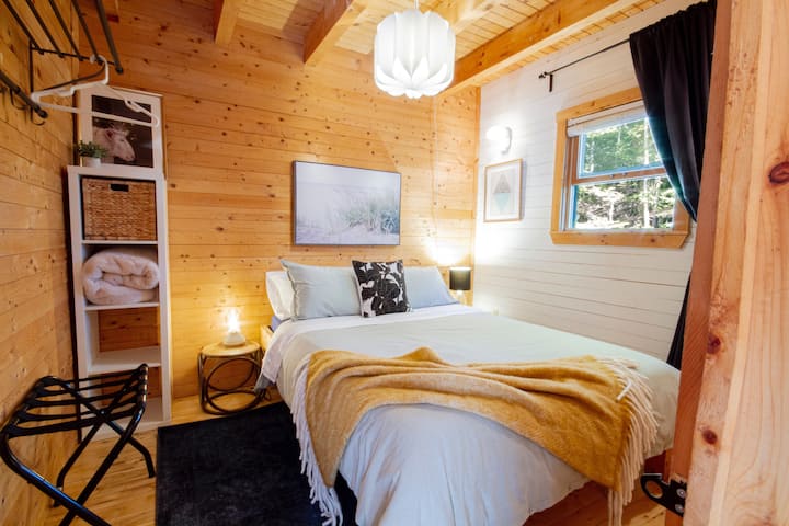 The main level bedroom has a queen size bed, luggage, and coat racks. 