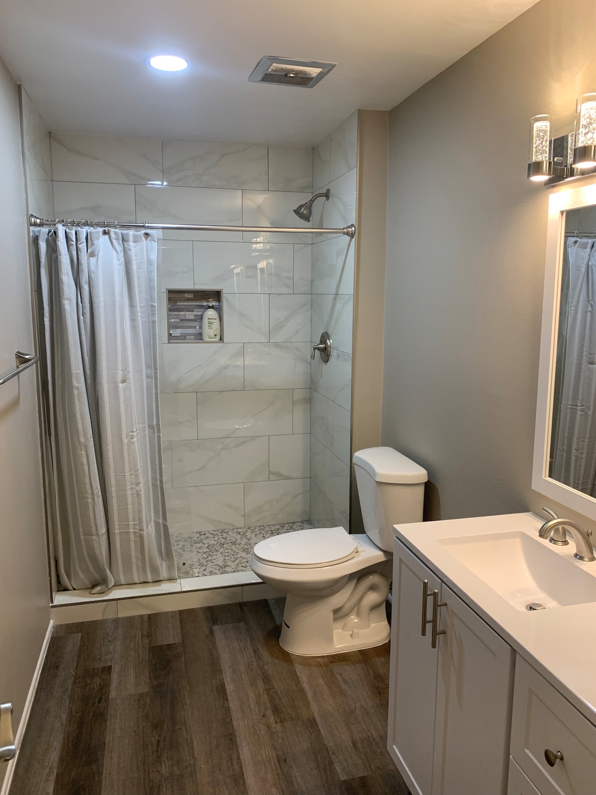 The bathroom features a modern shower with a glass door and a tiled interior. A white toilet is positioned beside a sleek vanity, which includes a sink and ample storage. Soft lighting illuminates the space, enhancing the clean lines and neutral color palette.