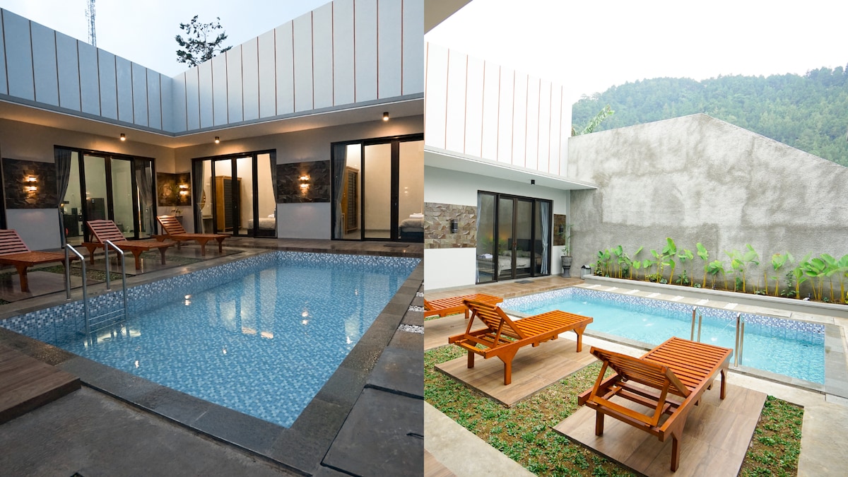 A serene swimming pool is framed by modern lounge chairs, inviting relaxation. Surrounding glass doors facilitate natural light and an open atmosphere. Lush greenery offers a tranquil backdrop, harmonizing with the contemporary design of the outdoor space.