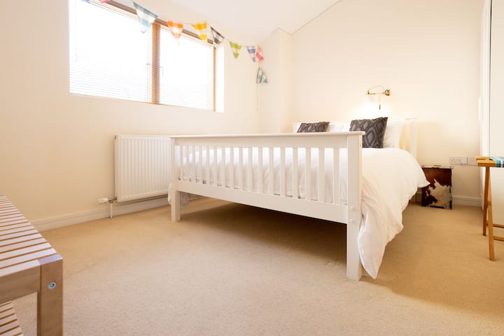 Chumba kikuu cha kulala katika Norwich Townhouse kina kitanda cha ukubwa wa mfalme na kina hewa na angavu. Chumba kinaonekana chini ya ua chini. Kuna nafasi kubwa ya mizigo na nguo.