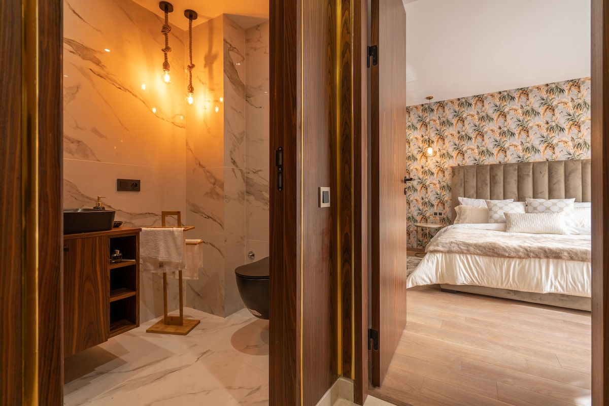 A doorway opens to reveal a modern bathroom featuring stylish lighting and marble finishes. Adjacent, a spacious bedroom is visible, adorned with floral wallpaper and a comfortable bed. Soft textures are highlighted, creating a harmonious blend of decor.