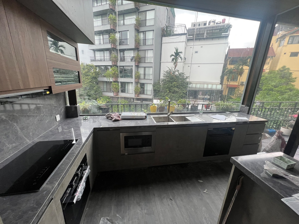 The kitchen features modern cabinetry and a sleek countertop with an integrated sink and stove. A large window offers a view of the surrounding greenery. Appliances include a built-in microwave and ample storage space is available throughout.