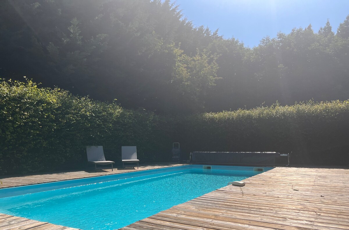 A private pool is surrounded by lush greenery, providing a serene environment. Wooden decking frames the pool, which is complemented by two lounge chairs positioned nearby. Natural light highlights the clear water, creating an inviting atmosphere for relaxation.