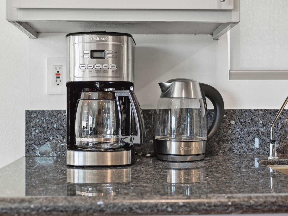 A modern kitchen countertop features a coffee maker with a glass carafe and a stainless steel kettle. The sleek granite surface provides a stylish backdrop, enhancing the convenience of beverage preparation.