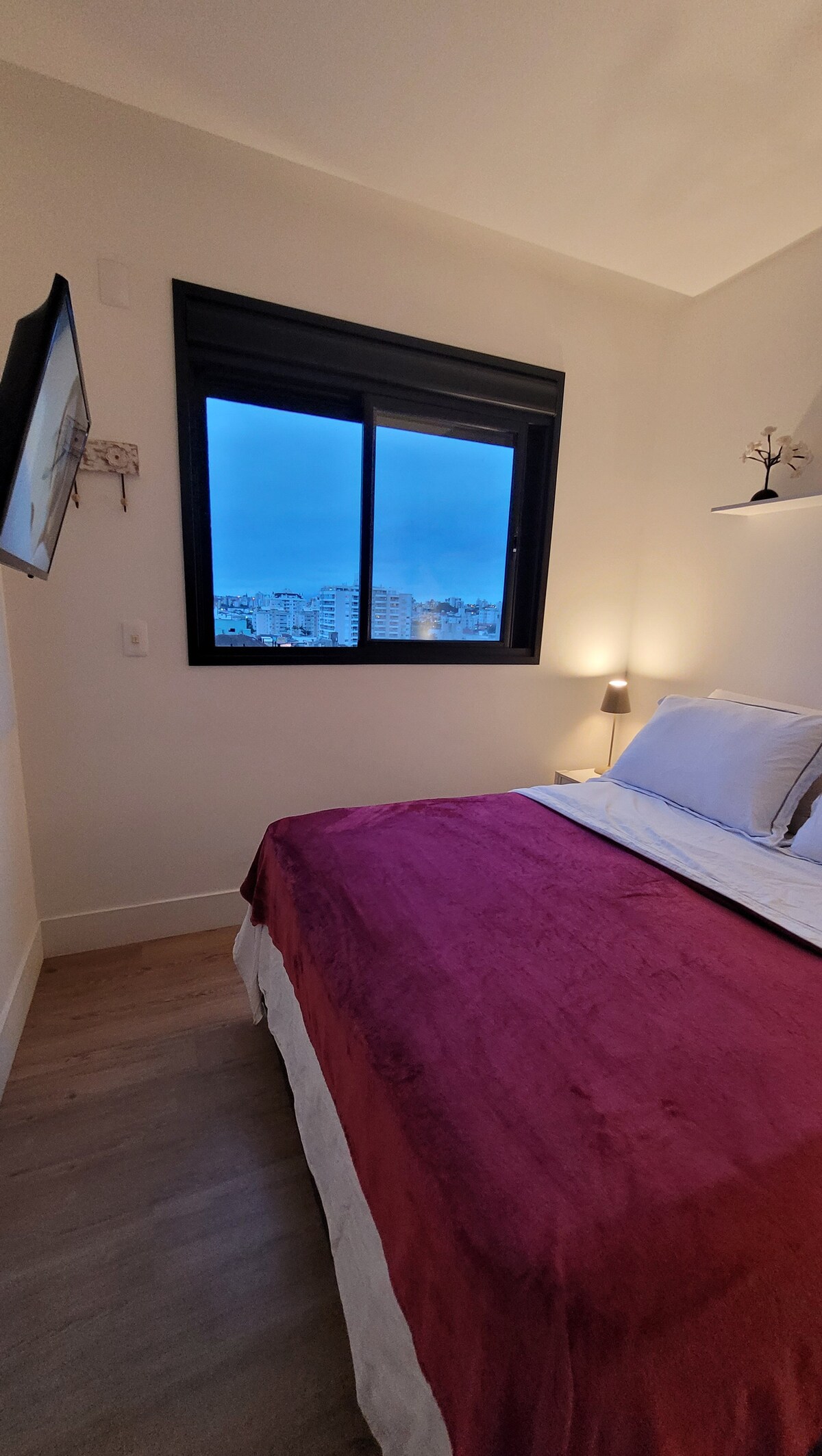 Cuarto con cama matrimonial, mesitas de noche, persianas, armario, ventana opaca y TV inteligente de 32 pulgadas.