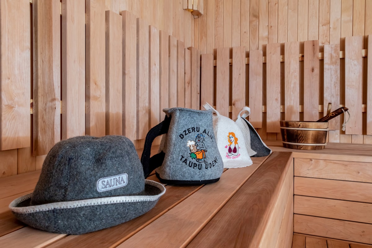 A wooden sauna interior showcases neatly arranged felt sauna hats and a decorative towel. The warm wood paneling and benches create a soothing atmosphere, complemented by a traditional wooden bucket in the background, reflecting a focus on wellness.