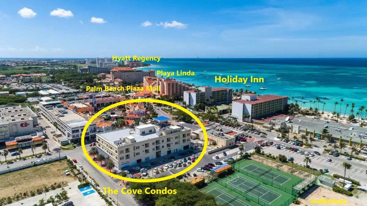 An aerial view showcases The Cove Condos, highlighted in a yellow circle. Surrounding buildings and landmarks, including the Holiday Inn and Hyatt Regency, can be seen. A stretch of blue ocean is visible in the background, with lush greenery framing the vibrant scene.