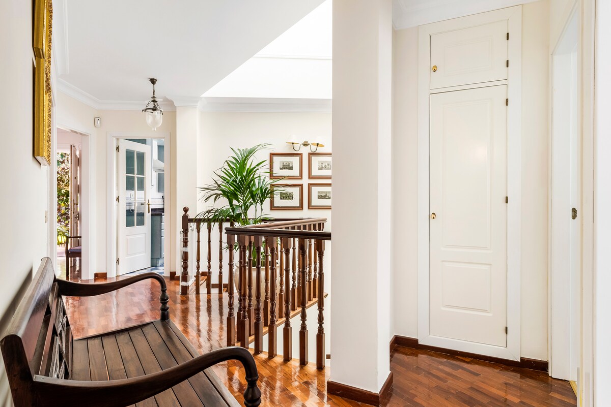 A welcoming hallway is featured, showcasing polished wooden floors and neutral-colored walls. A wooden bench is positioned against the wall, while a decorative plant adds a touch of greenery. Light enters through a skylight, enhancing the spacious feeling of the area.
