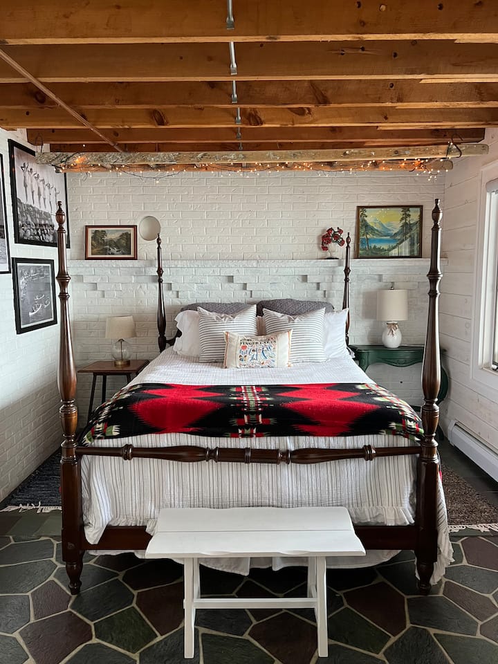 ห้องนอนชั้นใต้ดินพร้อมวิวทะเลสาบที่ยอดเยี่ยมรูปทะเลสาบวินเทจที่รักเรียงรายอยู่บนผนังและไฟระยิบระยับที่แขวนอยู่บนบันไดเหนือเตียงเป็นสัมผัสที่น่ารัก  